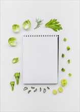 Varieties chopped vegetables surrounding spiral notepad white backdrop