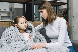 Mother taking care her daughter covered with gray woolen scarf suffering from fever