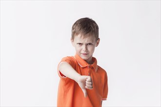Angry little boy showing dislike gesture white backdrop