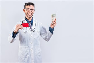 Handsome doctor holding money and credit cards isolated. Happy young doctor holding credit card and money isolated