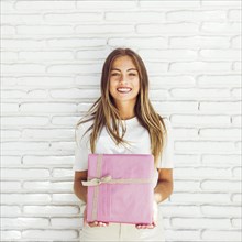 Smiling young woman holding pink gift box