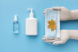 Top view hands holding medical mask with autumn leaf liquid soap bottle