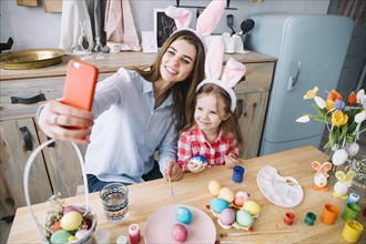 Young woman taking selfie with daughter near easter eggs