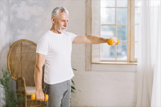 Fit senior man exercising with orange dumbbells home