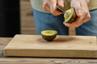 Closeup of male hand removing seed from avocado half with knife