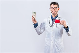Happy young doctor holding credit card and money isolated. Handsome doctor holding money and credit cards isolated