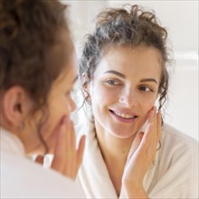 Woman applying cream face while looking mirror