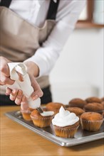 Young woman decorating cupcakes with white whipped cream by squeezing confectionery bag