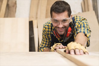 Happy male carpenter adjusting wooden plank workshop