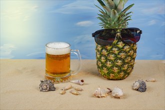Natural pineapple with sunglasses on the sand of the beach with a beer mug with foam