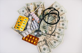 Top view of stethoscope with pills on money isolated. High cost of medical health with stethoscope and medicines. View of medical stethoscope with medicaments and money