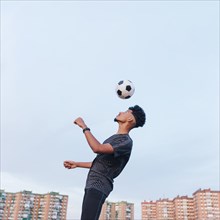 Male athlete training with soccer ball against blue sky
