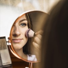 Hand mirror with reflection woman applying blusher her face