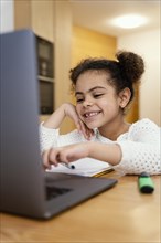 Happy little girl home during online school with laptop