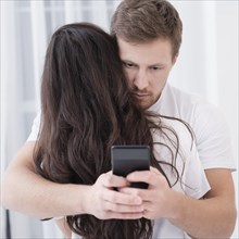Man hugging his girlfriend while checking his phone