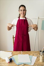 Portrait smiling young woman pointing fingers her red apron