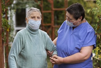 Female nurse taking care older woman with medical mask