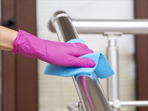Hand rail being disinfected by person with cloth surgical glove
