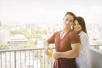 Happy woman hugging man with juice glass balcony