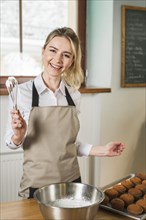 Smiling young woman holding cream with whisk coffee shop