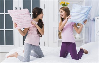 Two happy female friends doing pillow fight bed home