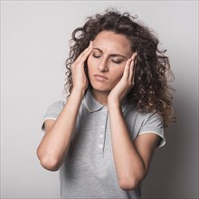 Woman with closed eyes having headache against gray background