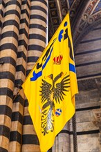 Black and white striped marble column of the cathedral with a Palio flag