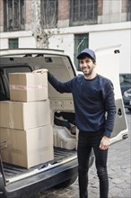 Portrait happy delivery man standing near vehicle with cardboard boxes
