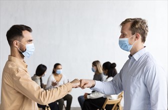 Men with medical masks fist bumping each other group therapy session