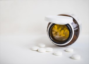 White round pills spilling from brown bottle white background