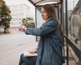 Woman waiting bus sitting with book her lap