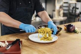 Male chef with gloves putting pasta plate