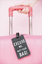 Person s hand holding handle travel suitcase with your bag tag against pink background