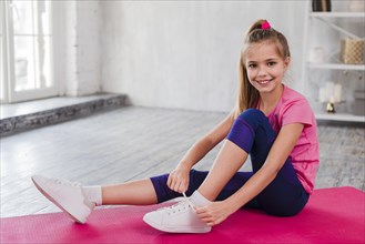 Portrait smiling girl sitting exercise mat tying her shoelace