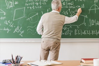 Aged math teacher writing equation chalkboard