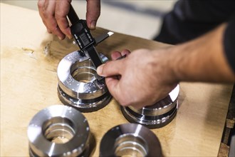 A man uses a digital caliper to measure the size of an opening in a metal part