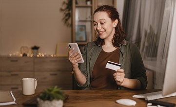 Smiley woman using her smartphone home with credit card