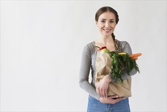 Smiley young woman holding paper bag with vegetables