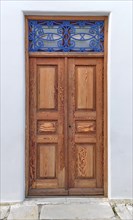 Old vintage wooden house doors in light natural color decorated with blue forge-smithing metal ornament with monograms of capital letters M and X. Whitewashed walls