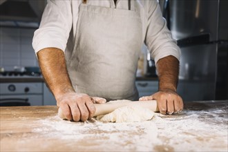 Close up male baker s hand flattening dough with rolling pin