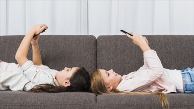 Happy female friends lying sofa using smart phone