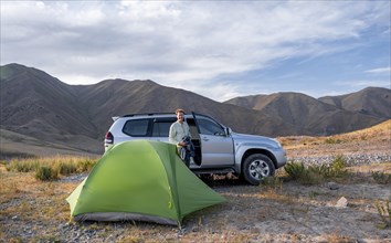 Tourist standing by a green tent and Toyota Land Cruiser four-wheel drive vehicle