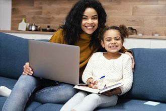 Smiley teenage girl helping little sister with online school laptop