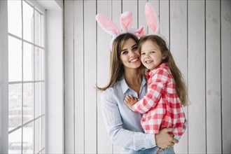 Young woman bunny ears holding daughter arms