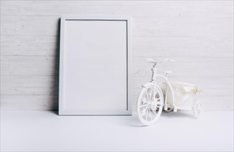 Empty white frame near bicycle white desk against wooden wall