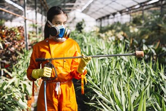 Female gardener with sprayer standing greenhouse