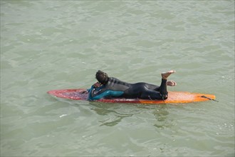 Surfer in wetsuit lying flat on his surfboard in the sea