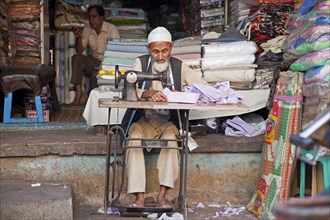 Tailor making clothes on old sewing machine in front of tailoring establishment
