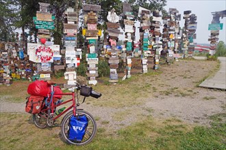 Various traffic and place signs face a bicycle loaded with luggage