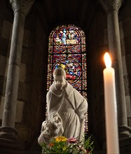 Interior photograph of saint figure in front of stained glass window